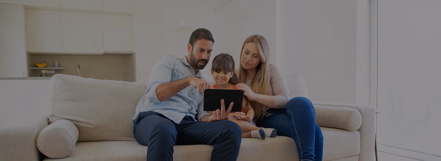 Familia reunida sentada no sofá, olhando para o tablet.
